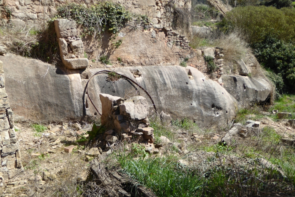 Roca de la cinglera amb encaixos d'antics coberts, al costat de la bassa semi-troglodítica