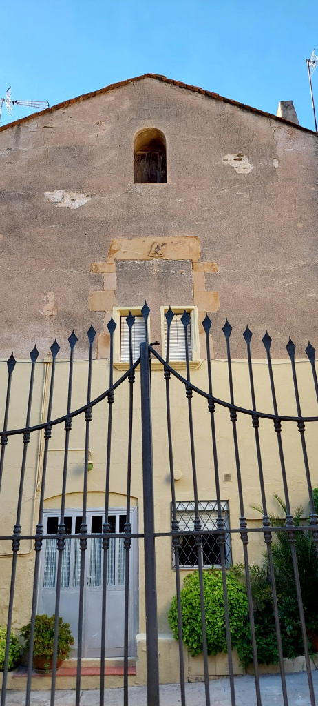 Antiga finestra de pedra que mostra a la llinda la campana, arma parlant de l'escut de la vila.