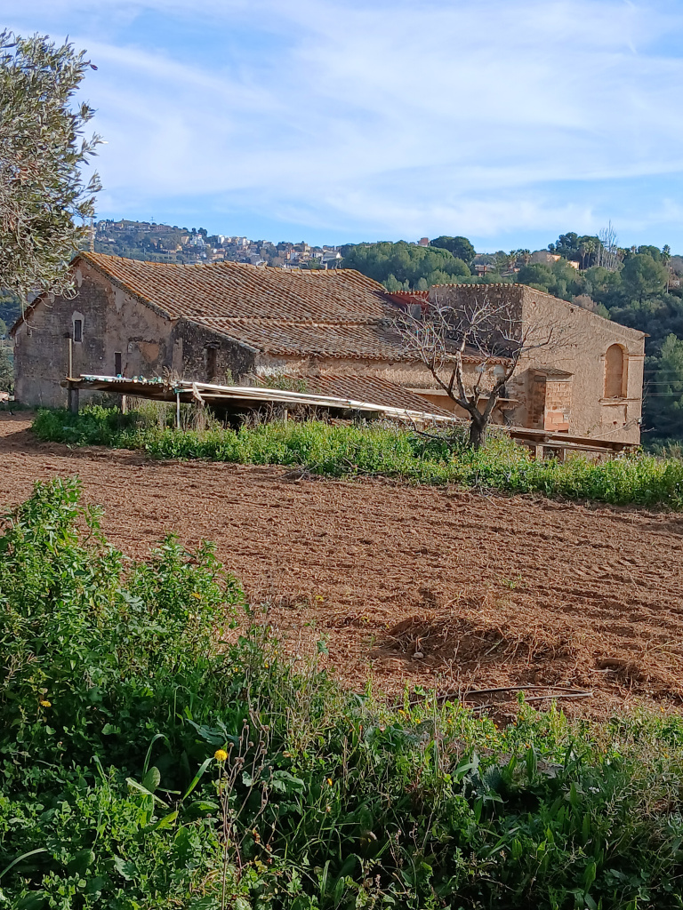Vista de la masia amb un camp de conreu llaurat en primer terme.