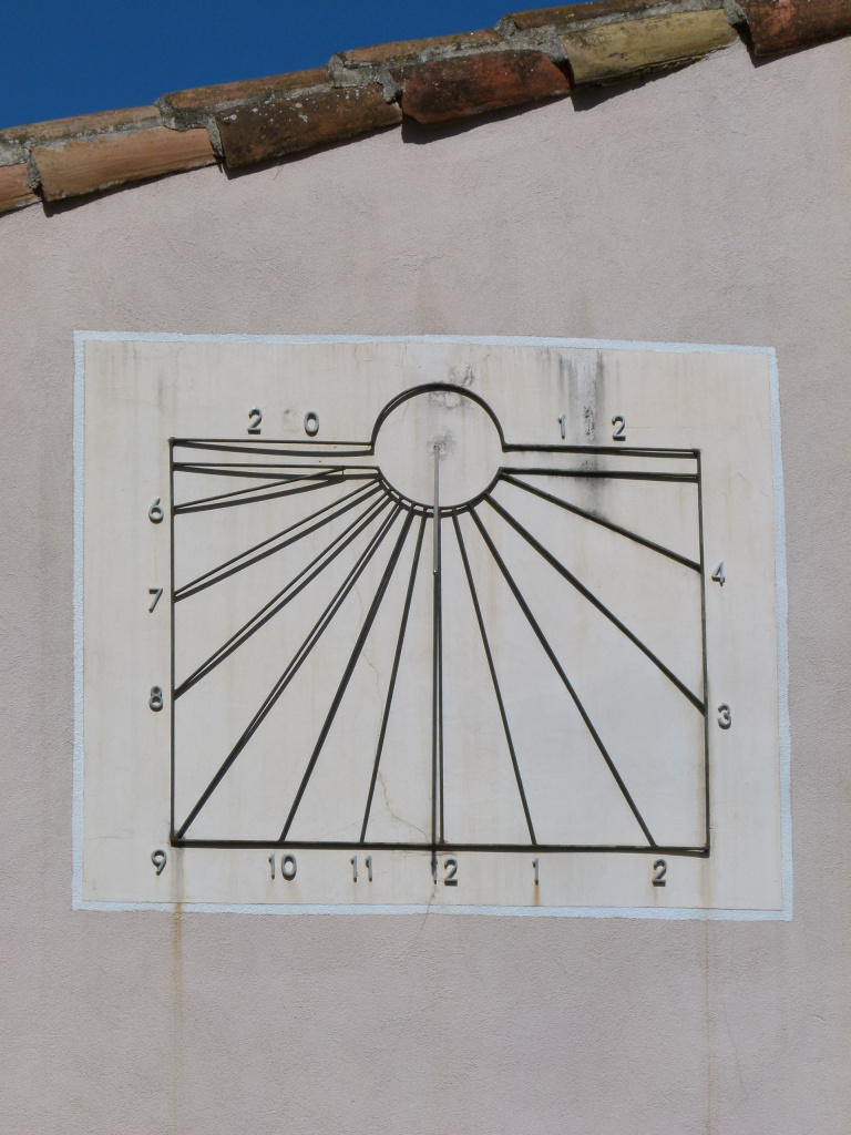 Detall del rellotge de sol metàl·lic amb el gnòmon projectant l’ombra sobre la superfície horària. A la part superior es llegueix la data de construcció: 2012.