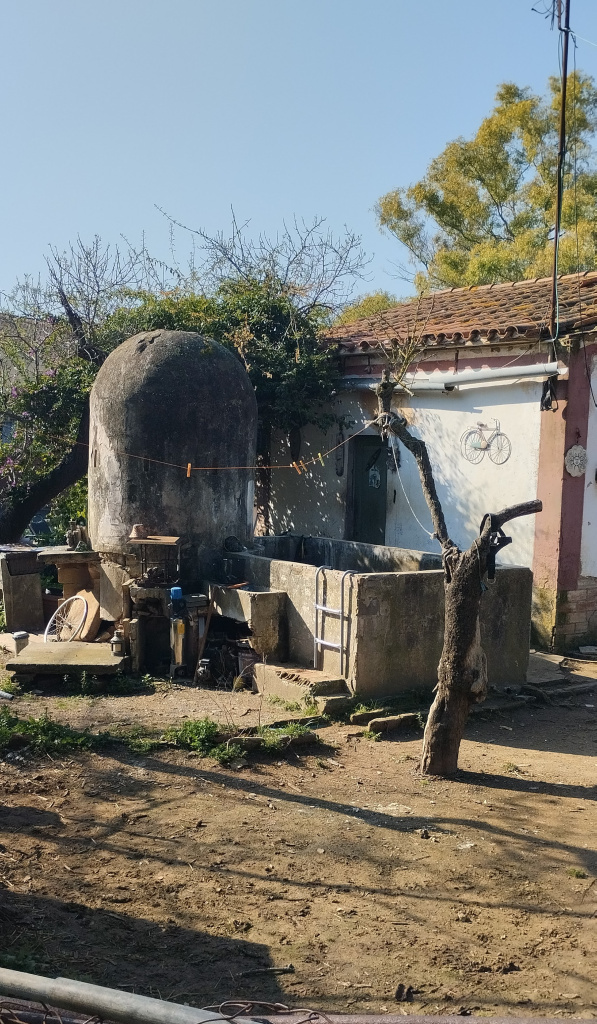 Vista del pou i el safareig amb la casa al fons.