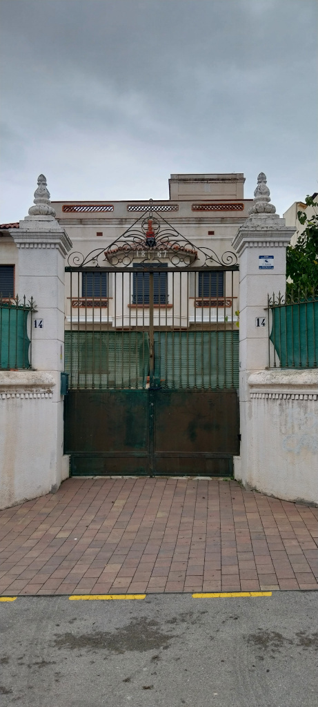 Vista general de la casa amb la tanca d'obra i la porta de forja en primer pla. 