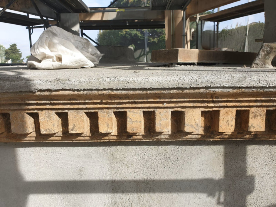 Detall del fris de la base de la construcció, amb decoració de dentells en el moment d'execució de la restauració de l'element. Font: DACarquitectura.