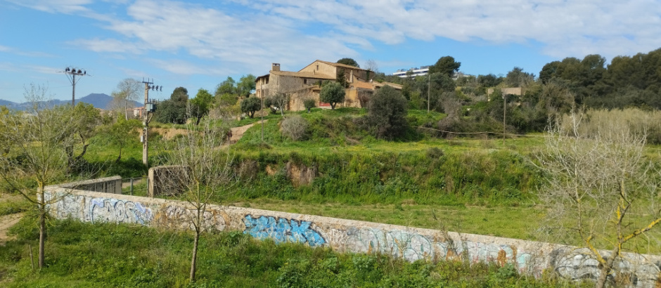 Vista dels horts amb la tanca de pedra en primer terme i el mas de can Gelabert al fons.