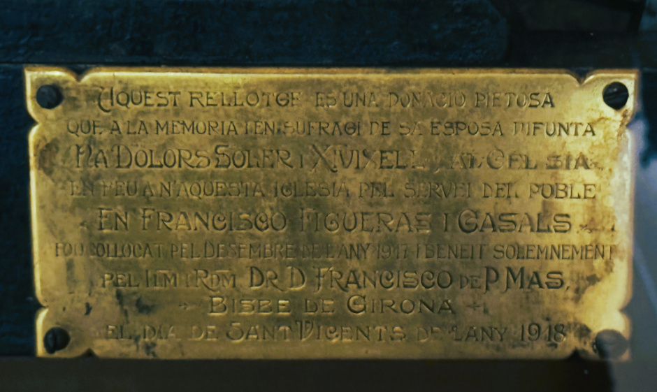 Placa a l'extrem dret de la base amb els benefactors del rellotge i la seva inauguració pel bisbe de Girona l'any 1918. 