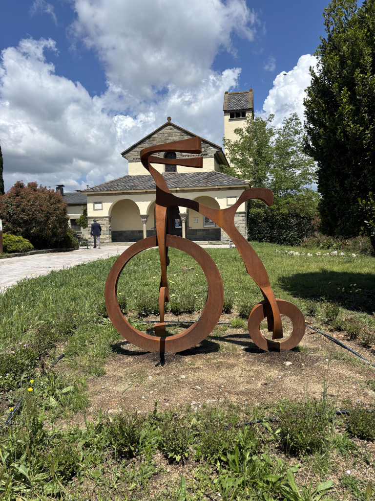 Imatge frontal de l'escultura on es pot veure la bicicleta i l'església nova al fons. Font: Fotografia pròpia