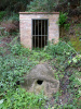 Vista de la caseta de boca mina amb la canalització i broc de la font en primer terme.